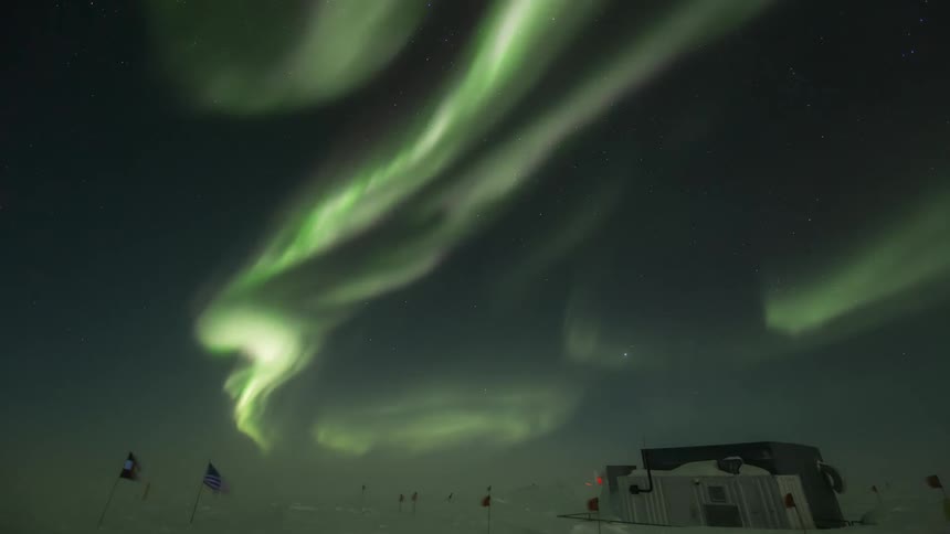 A beam of green light in the sky in a region with snow on the ground and a flag