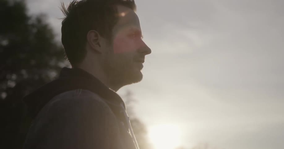 A man stands outside with the sun shining in the background
