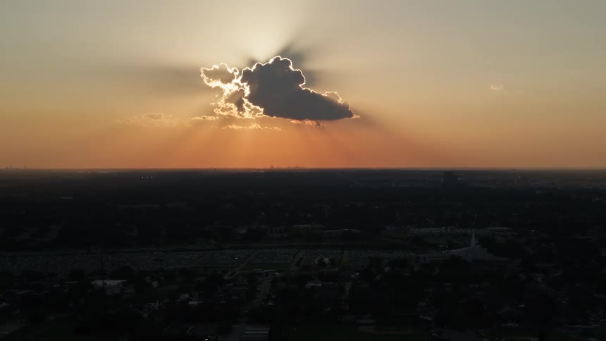 Sunlight outlines cloud obscuring the sun in a red tinted sky over an urban landscape