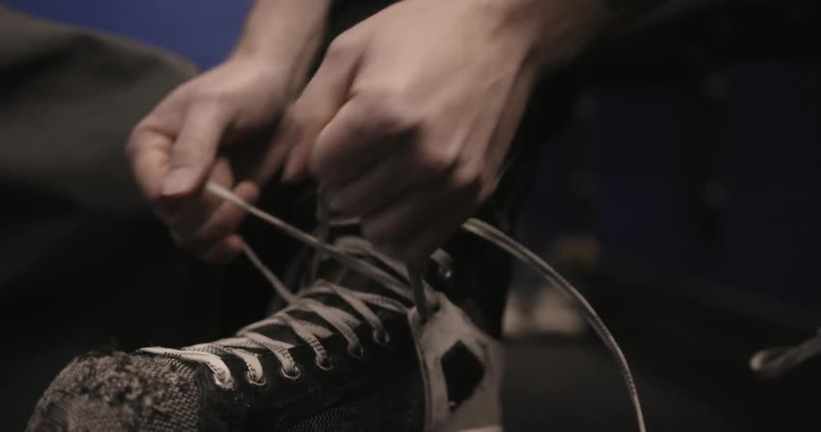 A man is lacing up a well worn pair of hockey skates