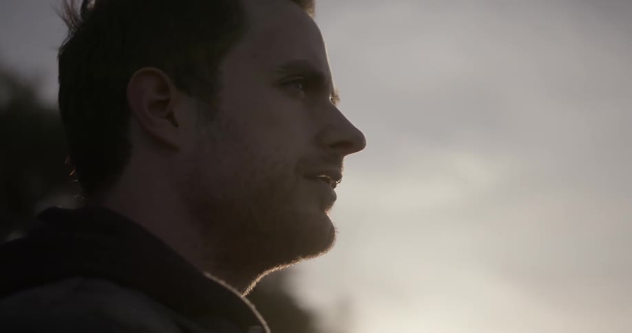 A man is standing outside at dusk and staring into the distance