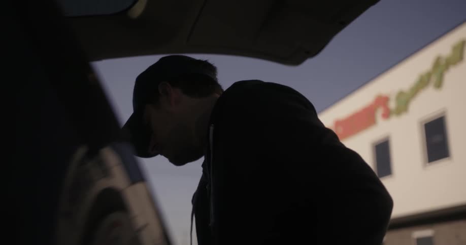 A man wearing a chicago cubs baseball cap opens the rear trunk of a car