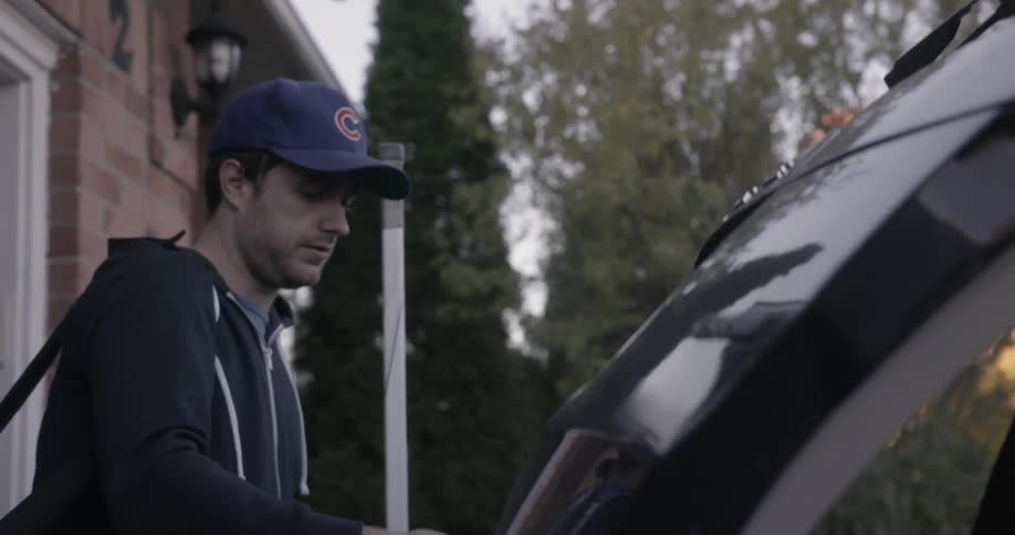 A man, carrying a bag, is opening up the trunk of the vehicle