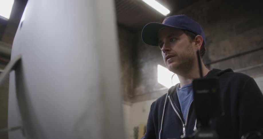A man wearing a baseball cap looks at a computer monitor