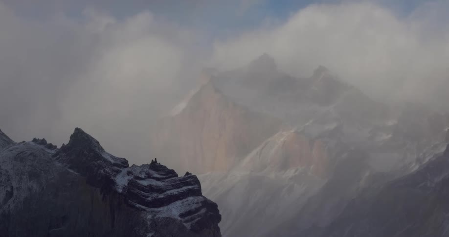 Snow dusts top of cliff across valley from cloud obscured mountain