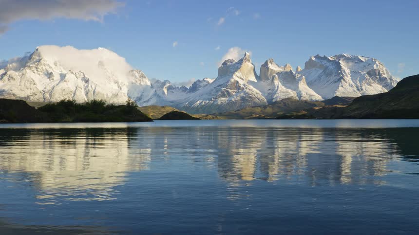 A landscape of a lake with some ripples reflecting the snowcovered mountains in the background