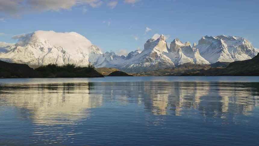 Rippling water reflects snow covered mountains on a cloudy day