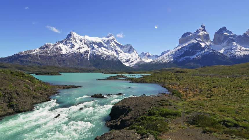 A large river flows through a valley surrounded by snow covered mountains