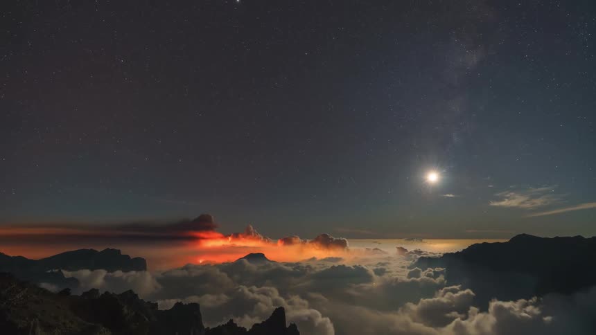 Time lapse footage of the night sky over a mountainous landscape and a volcano erupting
