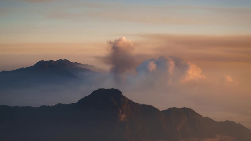 Clouds roil above foggy valley as setting sun tints sky red