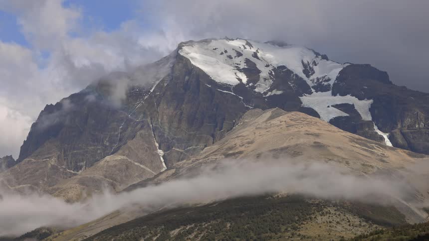 Time lapse of smoky clouds forming over a mountain peak behind another contrasting mountain side during the day