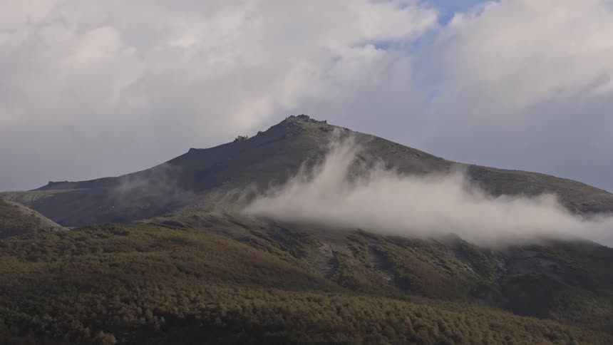 A large mountain with a huge white cloud passing in front of it