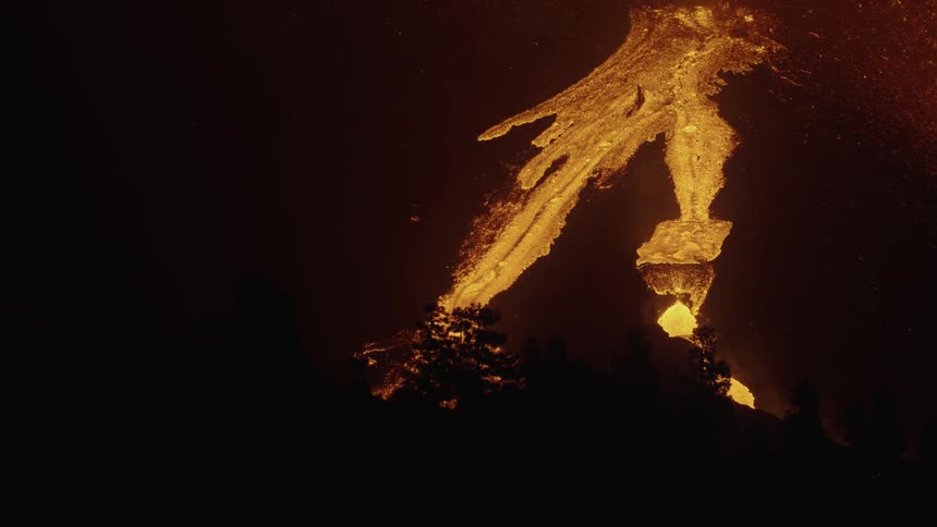 Lava flows down slope toward silhouetted trees at night