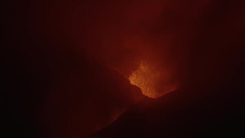 A fissure in a mountain with an erupting volcano that is spewing lava and magma upward