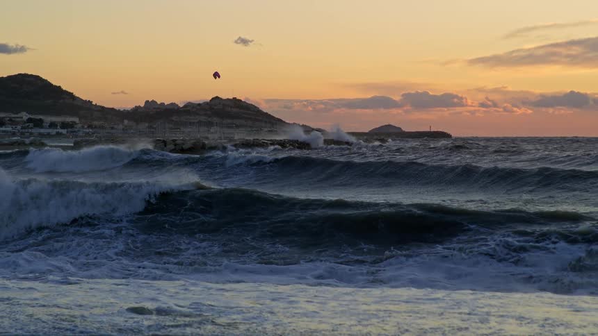 Person flies a kite on low lying islet as surf flows onto beach under a red sky