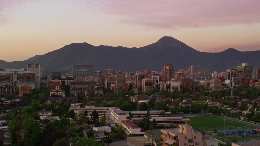 A city with tall buildings and lots of vegetation and behind it is a huge mountainous region
