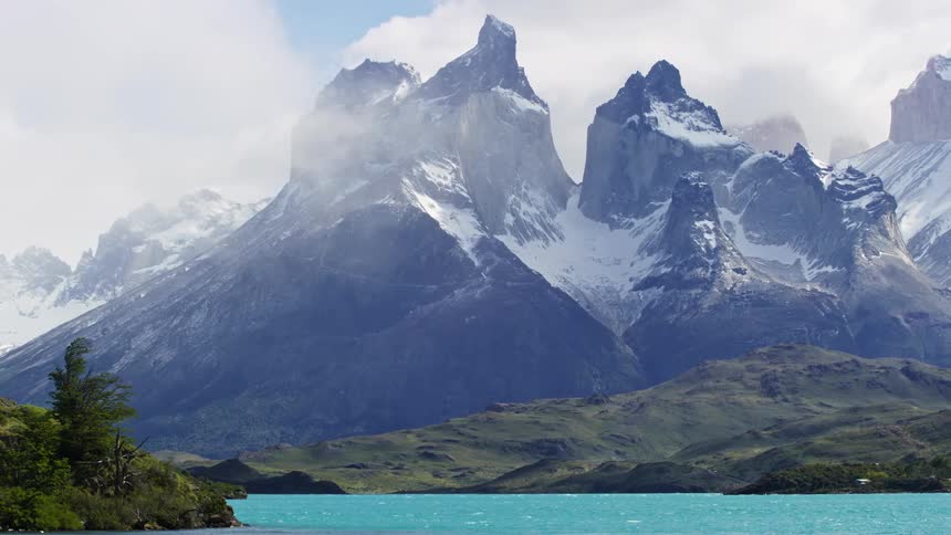 A landscape of high mountains with snowcapped peaks in front of a lake with clear water
