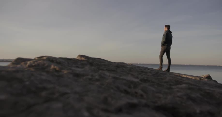 A man stands atop a hill staring out into the distance