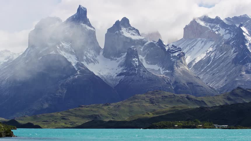 A rocky mountain range with snow at the peak of a clear river