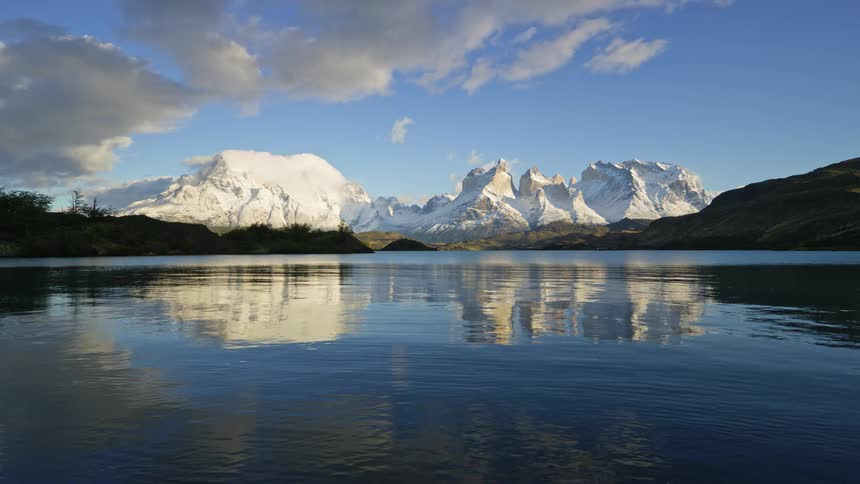 Timelapse of water rippling on a lake with white mountain peaks in the background and blue sky with white clouds reflecting from the water during the day