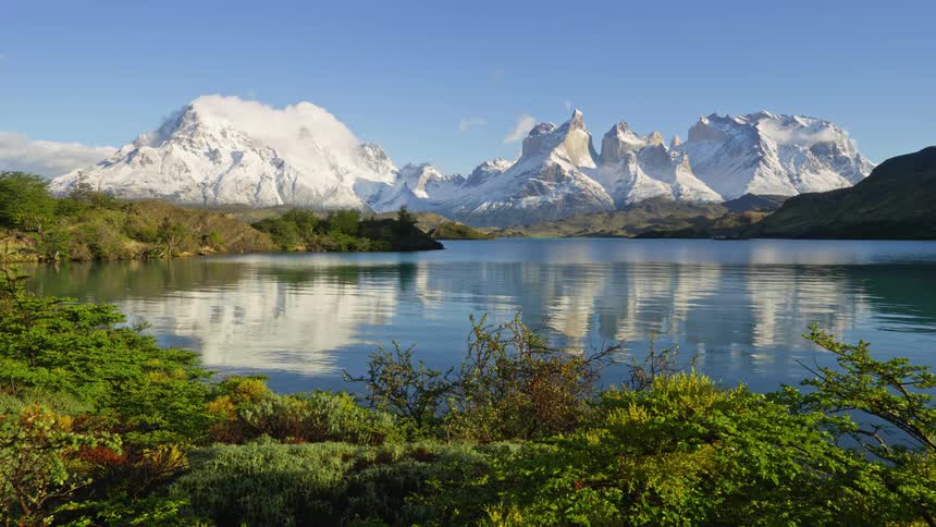 A placid lake between a grassy field and a snowy mountain range