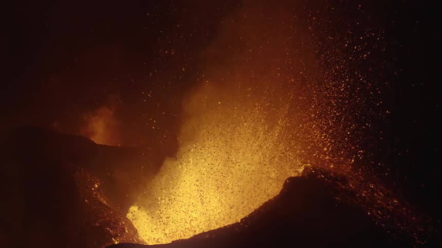 Lava sprays into the air from an erupting volcano as it glows in the darkness