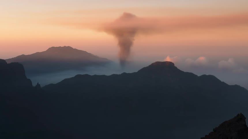 A volcano on top of a mountain is erupting releasing fire and lots of smoke