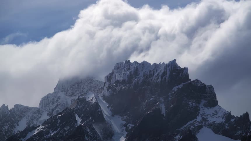 A huge mountain of rocks covered in ice and there is a big white cloud in the sky