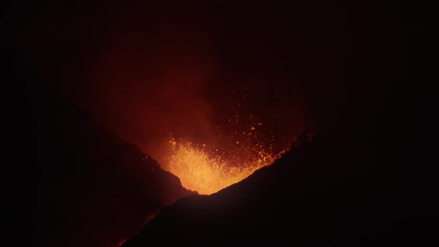 Lava sprays into the air from an erupting volcano as it glows in the darkness