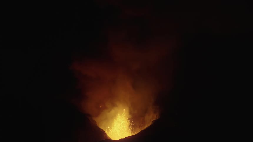 Lava spews forcefully into the night sky from an erupting volcano
