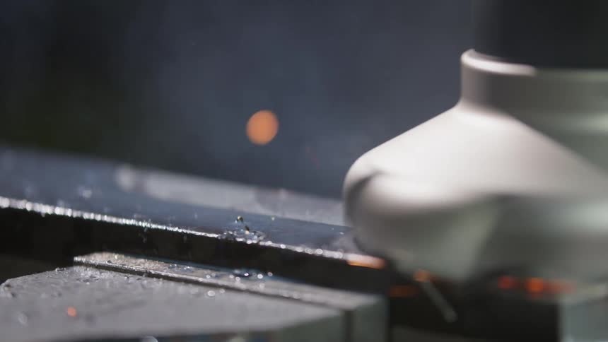 Rotating machine part creates sparks while shaving top of metal object in vise