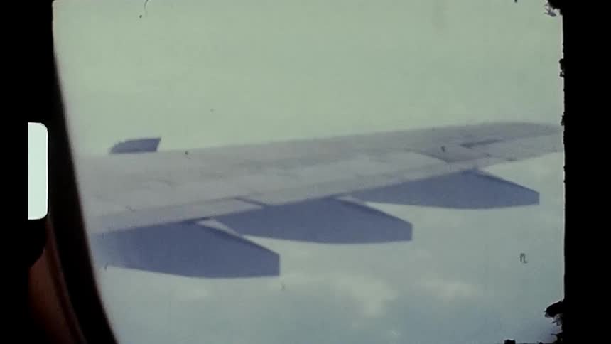 A wing of an airplane seen through a window with a clear sky outside caught on vintage film