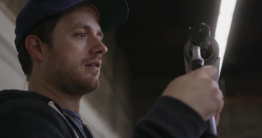A man wearing a baseball cap is sitting outside looking at something in his hands
