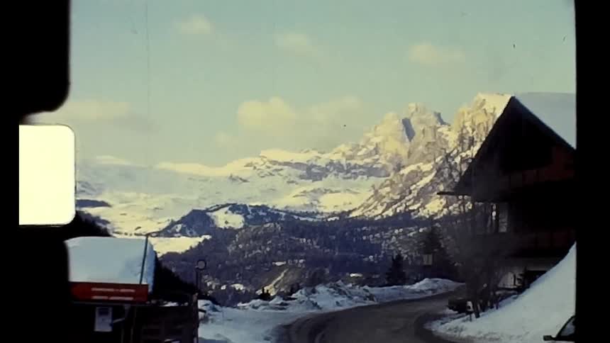 Car drives along road through town surrounded by mountains in winter