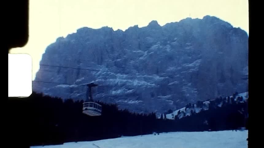 A cable car going down a cable in a region with snow on the ground and people skiing