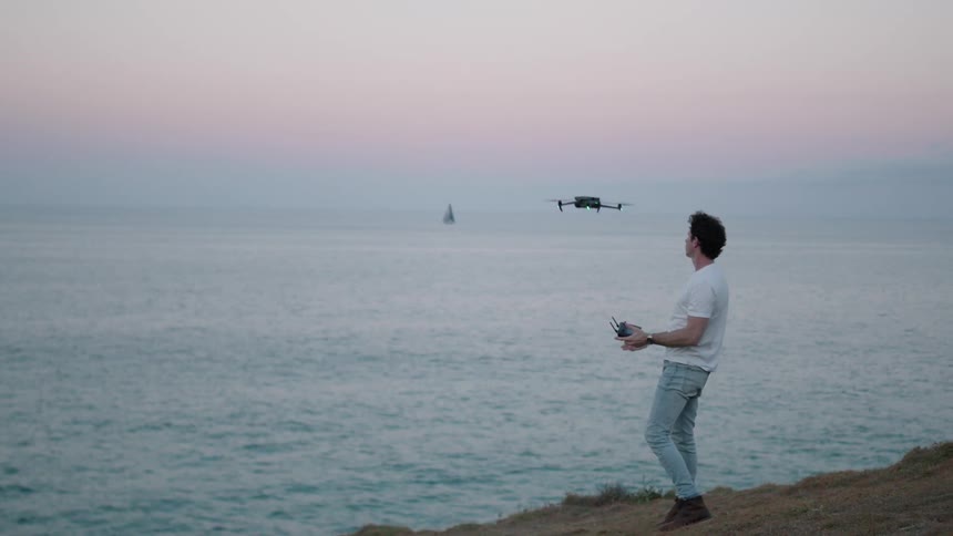 Man controlling a drone in the late afternoon next to the sea
