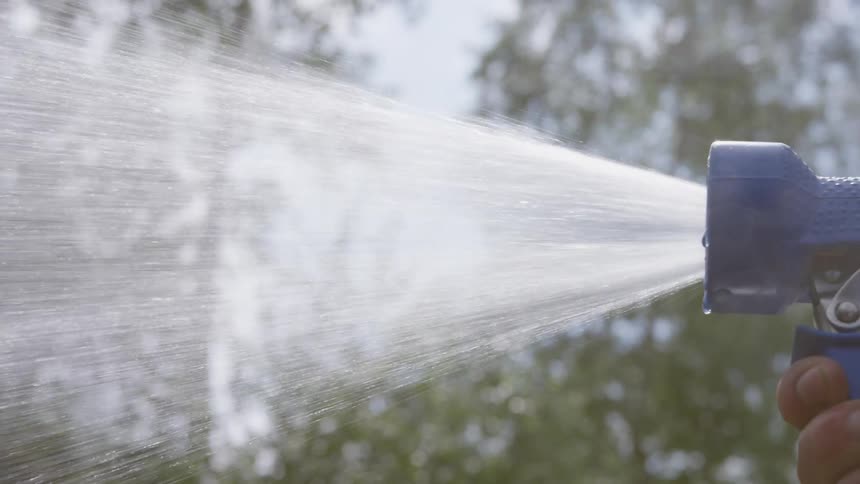 A hand holding a blue spray nozzle releasing a stream of water into the air