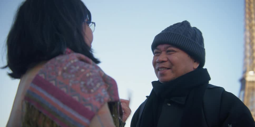 Two people are talking and wearing warm clothes near the eiffel tower