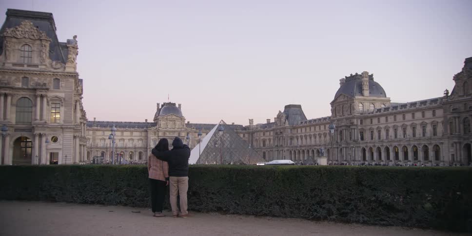 A couple looks at the louvre the man with his hand over the womans shoulder