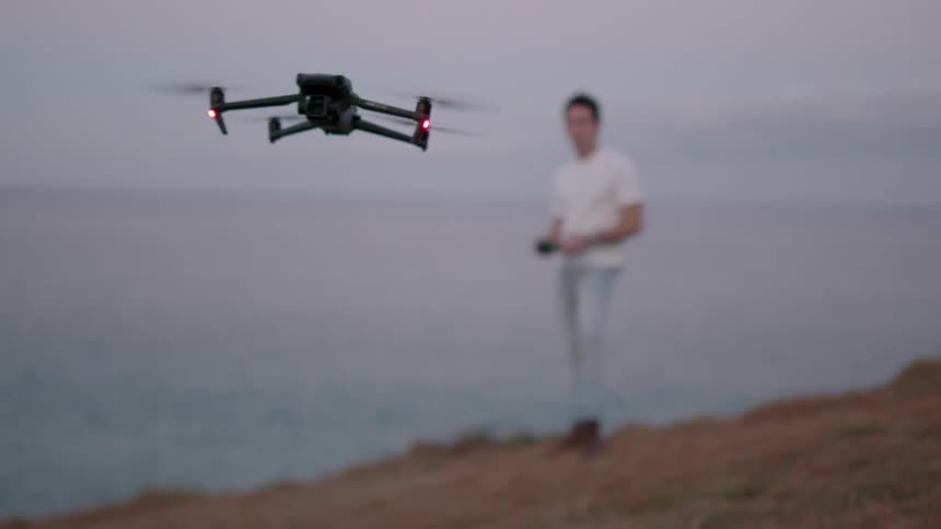 Man on the coast next to the sea controlling a drone