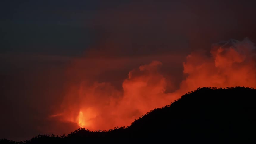 Glowing red smoke rises as a wildfire burns in a forested mountain valley