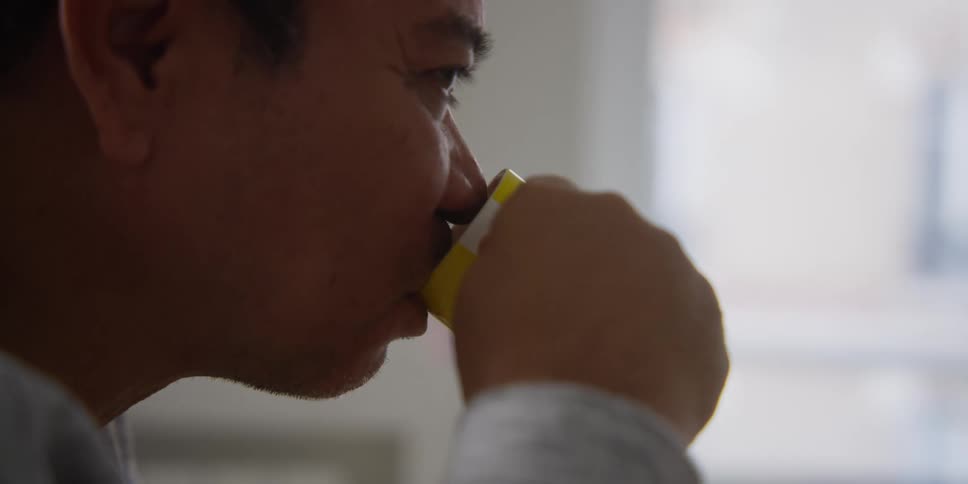 An asian man sips a drink out of a cup