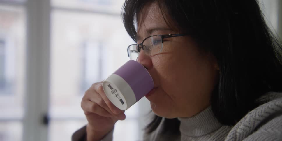 An asian drinks from a cup and smiles and talks