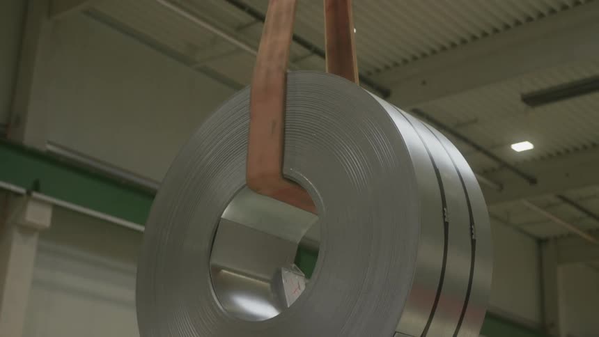 A suspended roll of steel being transported in a warehouse