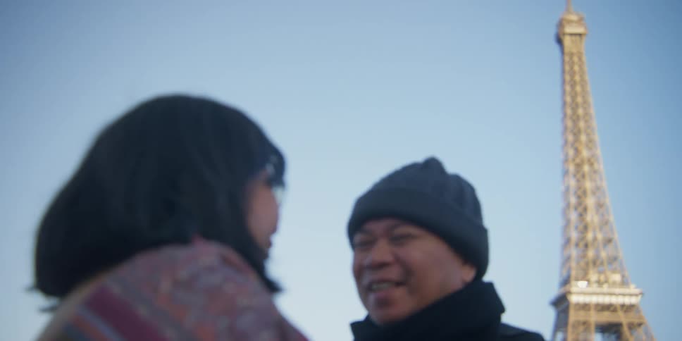 A couple speaks with each other while the eiffel tower stands tall in the background