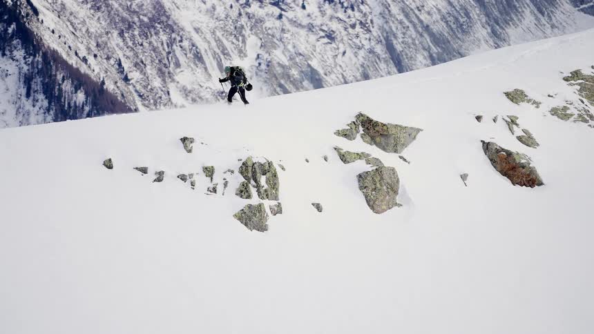 Person wearing backpack uses two walking sticks to hike across snow covered ridge in winter