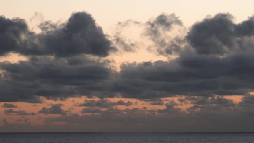 Several gray clouds passing in an orange sky in the morning