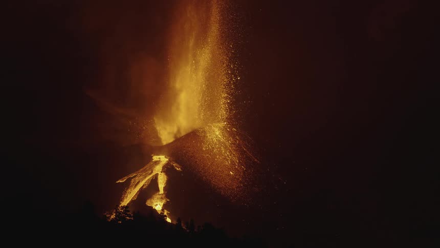 Lava sprays into the air as a volcano erupts and hot glowing lava flows