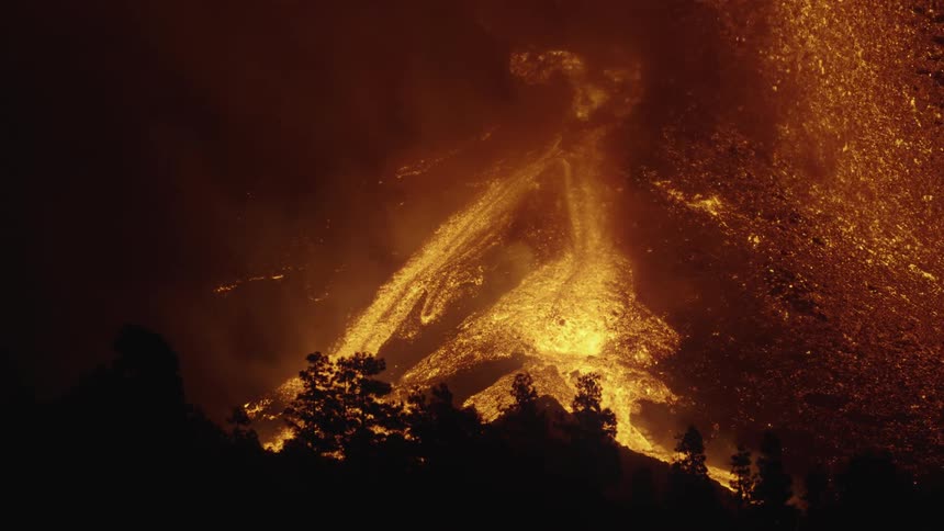 Volcano erupts as a hot glowing river of lava flows and splashes across the land
