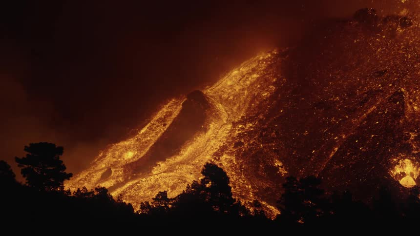Lava from an erupting volcano running down the surface of a mountain one night